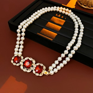 Close-up of double-layer pearl necklace featuring three large red crystals and gold finish