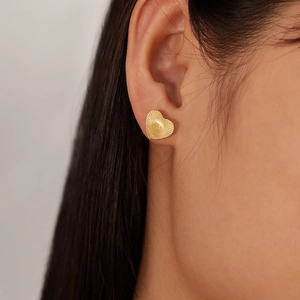 Detailed view of heart-shaped gold stud earrings with radial texture on a female model