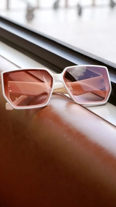 Detail view of white square sunglasses with pink gradient lenses on leather surface