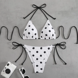 Flat lay of polka dot bikini set with halter top and side-tie bottoms on textured surface