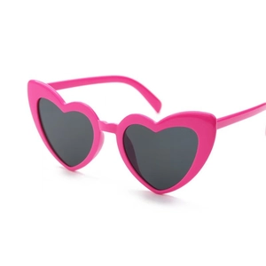 Detail of pink heart-shaped sunglasses featuring dark grey lenses and a plastic frame
