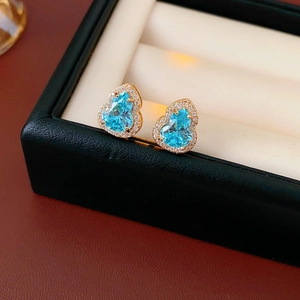 Macro shot of gold stud earrings featuring blue gourd-shaped stones and pavé set diamonds