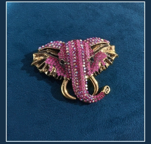 Detail of vintage golden elephant brooch with pink rhinestones on blue velvet background