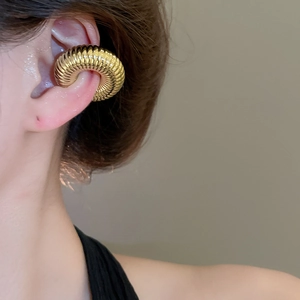 Gros plan d'un ear cuff doré à texture torsadée pour oreilles non percées