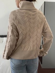 Detail of beige high-neck sweater showing intricate cable knit texture on the back