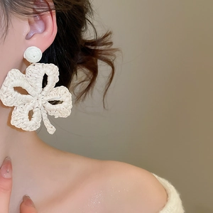 Close-up of a white raffia woven flower earring on a model for a summer vacation look