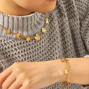 Golden five-petal flower titanium steel necklace and bracelet set on grey sweater