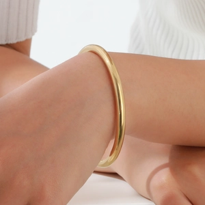 Close-up of a minimalist polished gold-plated stainless steel bangle worn on a model's wrist