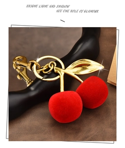 Macro detail of red flocked cherry keychain with gold leaf and lobster clasp on leather