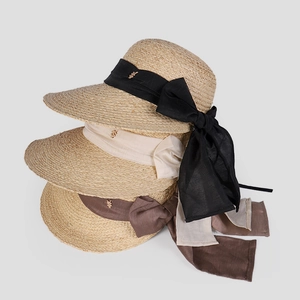 Détail de trois chapeaux en raphia en noir, crème et café avec des nœuds en ruban