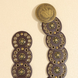 Detailed view of vintage brown leather disc belt with bronze rivets and embossed buckle