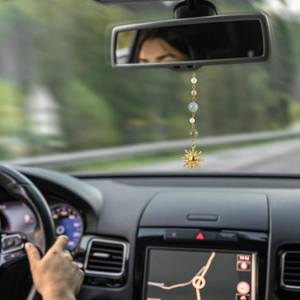 Detail of a sun-shaped car mirror charm with pearls and jade-like beads in a car interior