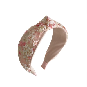 Pink mesh headband with floral embroidery and top knot design on white background