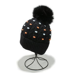 Detalle de un gorro de punto negro con lunares de colores y un gran pompón de piel sintética