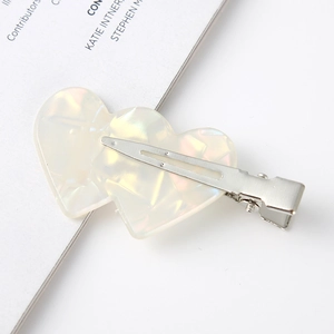 Close-up of heart-shaped acetate hair clip with iridescent pearl finish on metal alligator clip