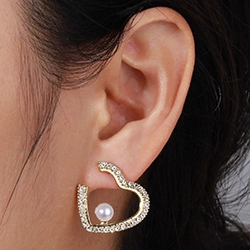 On-ear view of hollow gold heart earrings with sparkling crystals and a white pearl drop
