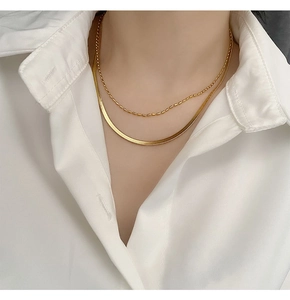 Detail of layered gold herringbone and bead necklaces on model neck over white shirt