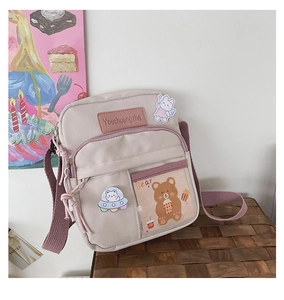 Détail du sac bandoulière en toile avec poche transparente, badges et étiquette chat