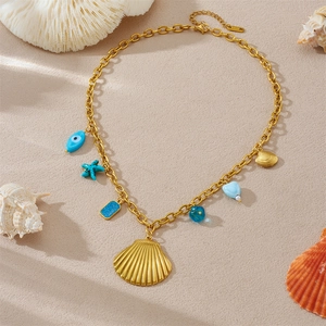 Detail der goldenen Muschelkette mit blauen Perlen auf Sand mit S.STEEL Gravur am Verschluss