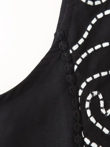 Detail of black cotton fabric featuring white embroidery and elegant pom-pom trim