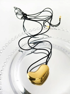 Detail of a 14K gold-plated bean pendant with smooth mirror finish on a black cord