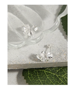 Detail of silver S925 ruffle earrings with metallic waves on grey stone and leaf
