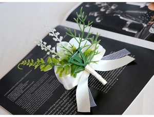 Detail of a handmade white fabric flower corsage with green leaves and a silk ribbon bow