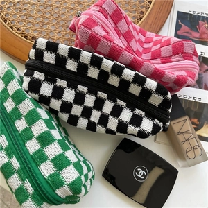 Three checkerboard knit cosmetic bags in pink, black, and green on a woven tray