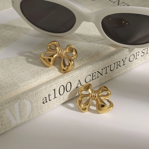 Macro view of golden bow earrings on book spine, elegant stainless steel jewelry detail