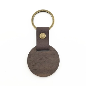Detail of round walnut wood keychain with brown leather strap and brass ring buckle