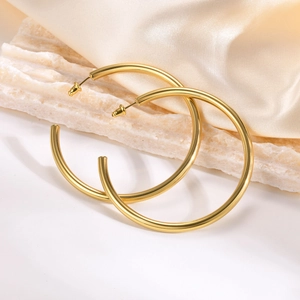 Polished gold hollow C-shape hoop earrings on white stone and champagne silk background