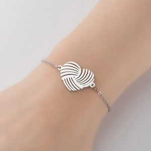 Close-up of a silver stainless steel chain bracelet with a woven heart pendant on a wrist