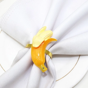 Close-up of a yellow banana napkin ring on a white cloth napkin with gold rim plate
