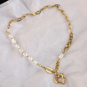 Gold paperclip chain necklace with baroque pearls and heart pendant on white paper