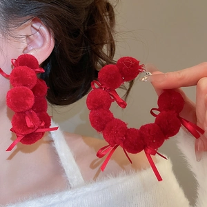 Detail of red plush ball hoop earrings with velvet ribbon bow shown on a model