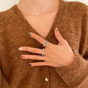 Close-up of a silver pearl necklace and heart ring set on a brown knitted sweater
