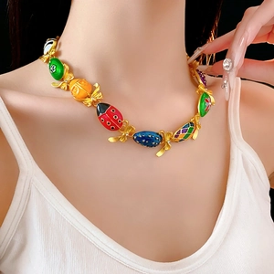 Dettaglio di una collana vintage in smalto con coccinella e caramelle su oro