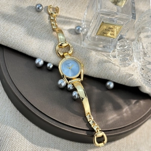 Close-up of women's gold horseshoe watch with blue dial on elegant fabric with accessories