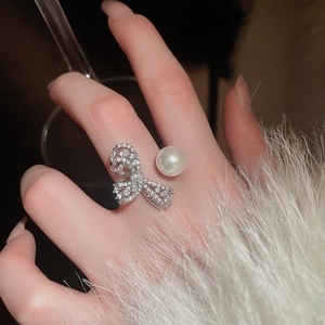 Macro detail of silver zircon bow ring featuring a white pearl on a model finger