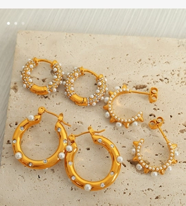 Three-piece gold earring set with pearls and crystals on beige stone background