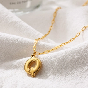 Macro shot of 3D bubble letter Q pendant in gold finish on a delicate cable chain