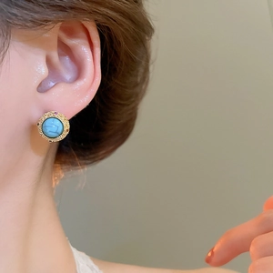 Close-up of vintage round turquoise stud earrings with textured gold plating on model