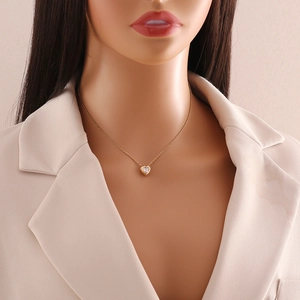 Elegant gold heart pendant necklace with clear gemstone worn on a model with a beige suit