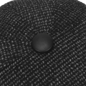 Macro detail of charcoal tweed fabric and premium black leather button on winter cap
