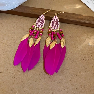 Detail of bohemian earrings with pink feathers, golden alloy leaves, and beaded tassels