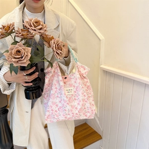 Detail of pink floral canvas tote bag held by model featuring brand label and texture