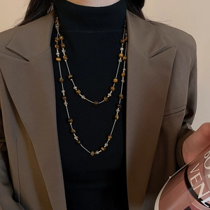 Detailed view of a vintage tiger eye beaded necklace layered on a brown blazer outfit