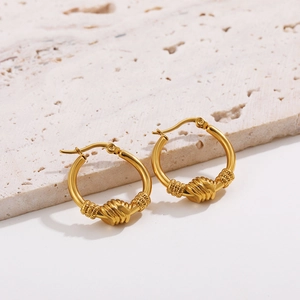 Close-up of golden hollow earrings with woven knot detail on a textured stone base