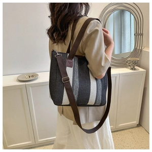 Detail view of a striped tote bag with brown fabric straps worn over a khaki blazer