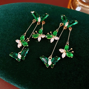 Détail macro de boucles d'oreilles papillon émeraude avec pompons dorés sur velours